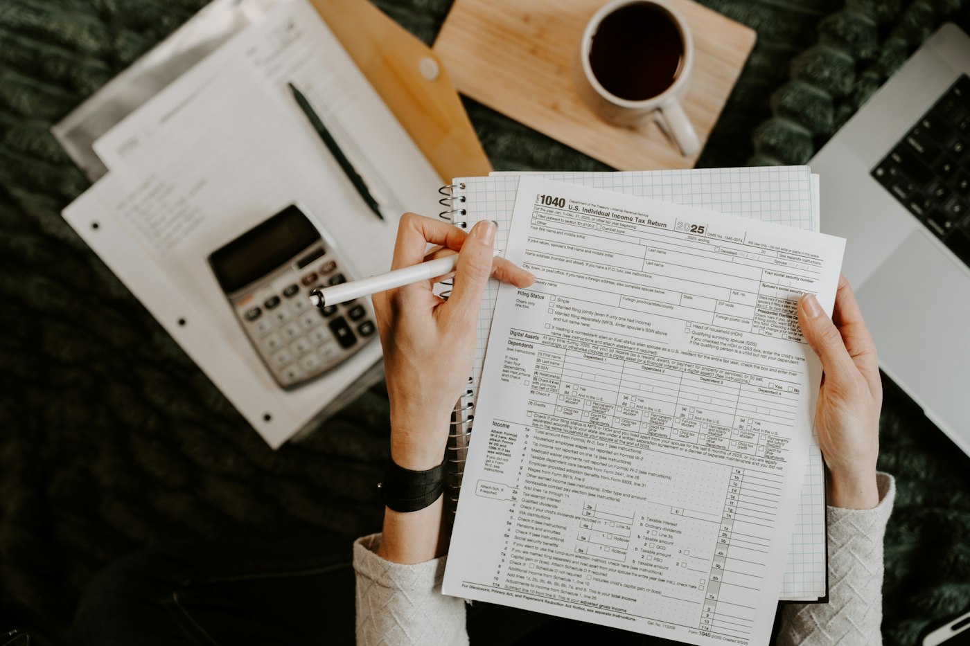Hands filling in a tax form beside a calculator and laptop